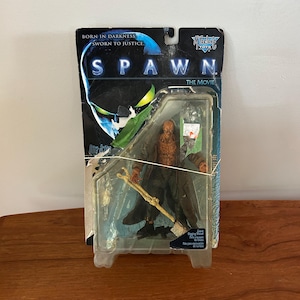 May include: A Spawn action figure from the film, still in its original packaging. The packaging features the words "Spawn The Movie" and "Born in Darkness Sworn to Justice." The figure is brown and black, with a staff.