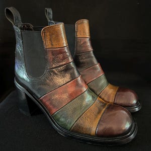 Puede incluir: Botines de cuero coloridos con tacón de bloque. Los botines presentan un diseño de patchwork con rayas horizontales en tonos marrón, verde, rojo y beige. Tienen una lengüeta en la parte trasera y paneles laterales elásticos.