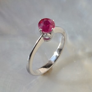 May include: A silver ring with a red ruby gemstone set in a prong setting.