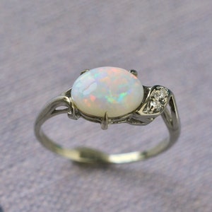 May include: A silver ring with a white opal gemstone and two small diamonds set in a leaf-like design.