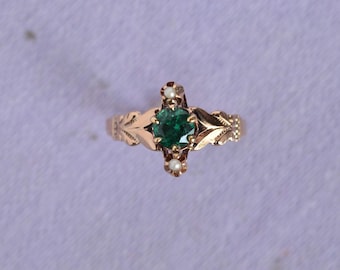 May include: A gold ring with a green gemstone and three small white pearls. The ring has a delicate floral design.