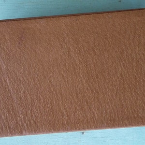 May include: A rectangular, brown leather box with a textured surface. The box has a simple, classic design and appears to be well-made. The color is a warm, medium brown, and the edges are slightly rounded.