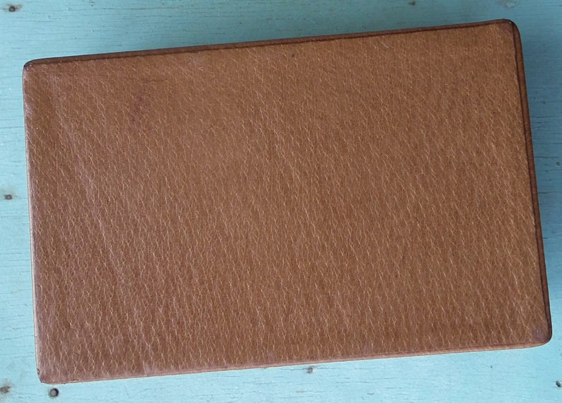 May include: A rectangular, brown leather box with a textured surface. The box has a simple, classic design and appears to be well-made. The color is a warm, medium brown, and the edges are slightly rounded.
