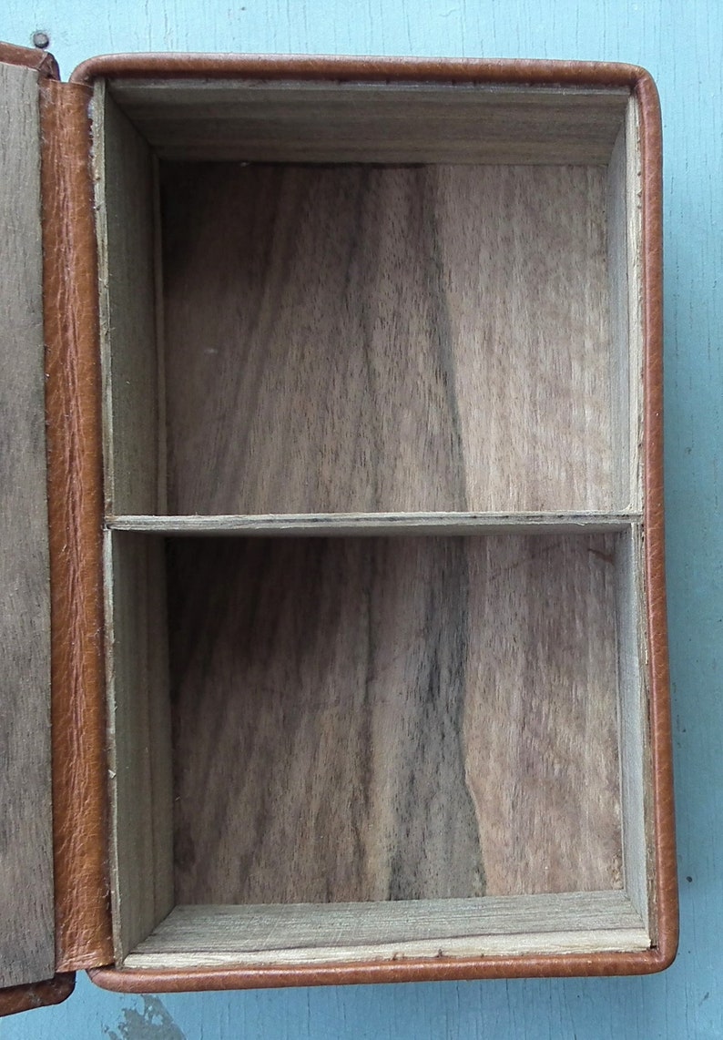 May include: Open, rectangular wooden box with a light brown leather exterior. The interior is divided into two compartments by a horizontal shelf. The wood grain is visible inside the box.