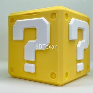 May include: A yellow cube with white question marks on each side. The text "3DTexan" is visible on the side of the cube. The cube has a rounded top and appears to be 3D-printed.