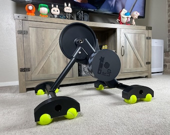 May include: Black exercise equipment with a large flywheel and the text "Crank It Up". The equipment has black legs with yellow tennis balls attached to the bottom. The equipment is on a carpeted floor.