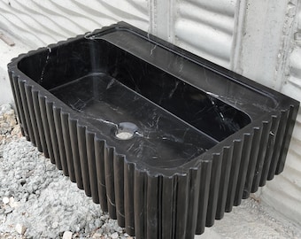 May include: Black marble sink with a fluted design. The sink is rectangular and has a drain hole in the center.