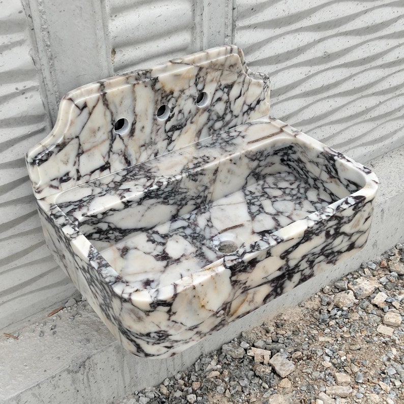 Close up of a Calacatta Viola marble sink with striking violet veining and a matching backsplash, showcasing luxury craftsmanship.