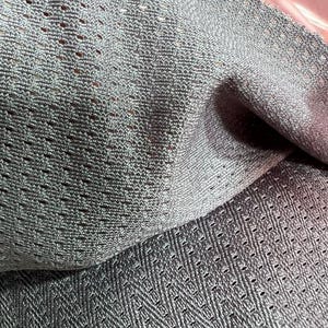 May include: A grey fabric with a distinct mesh texture featuring a repeating diamond-shaped pattern of small perforations. The material has a slight sheen and is folded to show the depth of the weave and the consistent grid-like structure.
