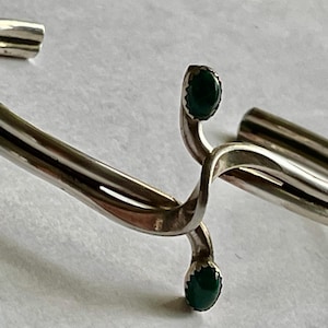 May include: A silver bracelet with a twisted design and two green stones.