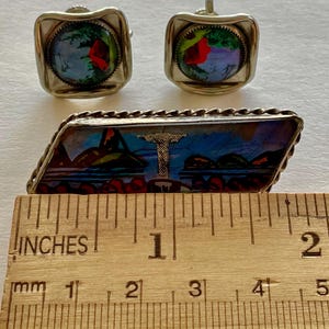 May include: A set of vintage jewellery, including a pair of square cufflinks and a rectangular brooch. The cufflinks and brooch feature a colourful, iridescent design. The brooch is approximately 5 cm long.
