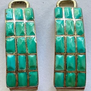 Op de afbeelding: Een paar rechthoekige oorbellen met een zilverkleurig metalen frame. Elke oorbel is versierd met turquoise rechthoekige stenen gerangschikt in een rasterpatroon. Ze hebben een kleine, gebogen zilveren lus aan de bovenkant.