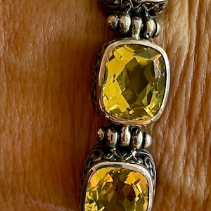 Könnte beinhalten: Ein silbernes Armband mit drei großen, quadratischen, gelben Edelsteinen. Das Armband hat ein zartes, verziertes Design.