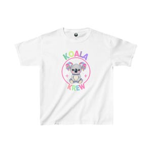 May include: White t-shirt featuring a colorful graphic of a koala bear with rainbow-colored ears and the text "KOALA KREW" in pastel colors. The design is centered on the front of the shirt.