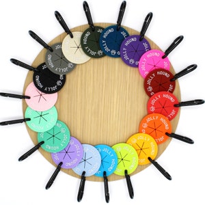 May include: A set of 12 colourful round dog tags with the words "Jolly Hound" printed on them. The tags are attached to a wooden circle with metal rings.