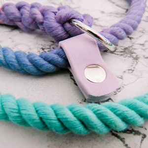 Pode incluir: Uma trela de corda colorida para c&atilde;es com um esquema de cores roxo, azul e turquesa. A trela tem um anel de metal prateado e uma al&ccedil;a de couro lavanda com um bot&atilde;o prateado.