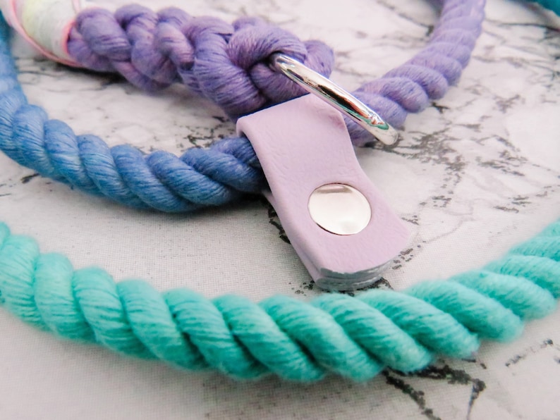Pode incluir: Uma trela de corda colorida para c&atilde;es com um esquema de cores roxo, azul e turquesa. A trela tem um anel de metal prateado e uma al&ccedil;a de couro lavanda com um bot&atilde;o prateado.