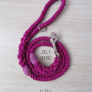 May include: A pink cotton rope dog leash with a silver clip and a silver ring. The leash is coiled and the brand name "JOLLY HOOUND" is printed on the rope. The word "BERRY" is printed below the leash.