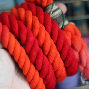 May include: A thick, multi-colored rope made of cotton. The rope is red, orange, and yellow. It is twisted together in a spiral pattern.