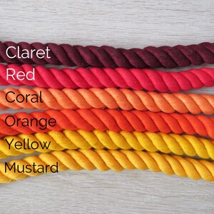 Pode incluir: Seis rolos de corda de algod&atilde;o em v&aacute;rios tons de vermelho, laranja e amarelo. As cores s&atilde;o, de cima para baixo, vinho tinto, vermelho, coral, laranja, amarelo e mostarda.