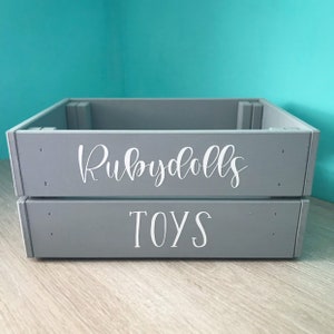 May include: A gray wooden storage box with the words "Rubydolls Toys" written in white on the front.