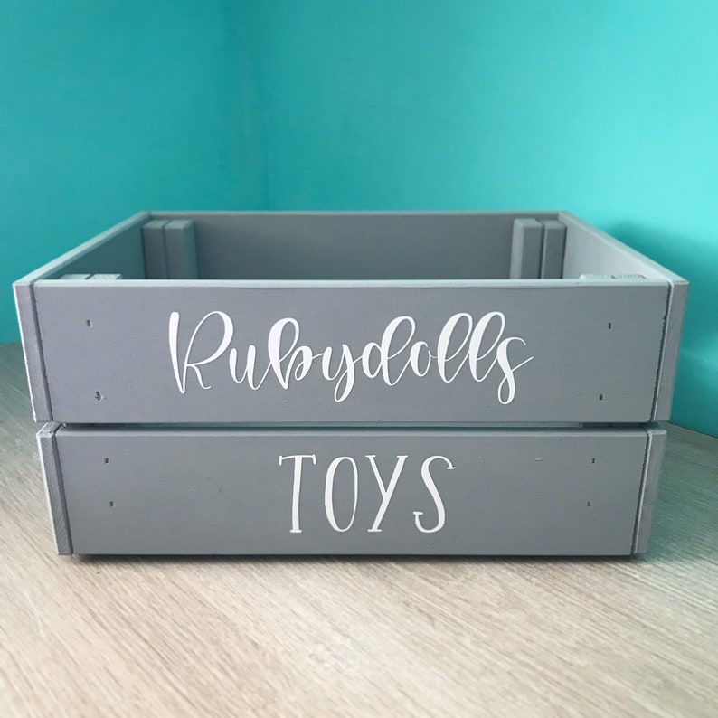 May include: A gray wooden storage box with the words "Rubydolls Toys" written in white on the front.