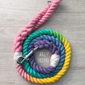 May include: A pastel rainbow colored rope dog leash with a silver clip. The leash is made of thick, braided rope and has a  "JOLLY HOOUND" label on the purple section. The text "PASTEL RAINBOW" is printed below the leash.