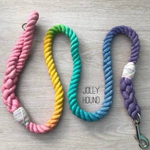 May include: Three colorful rope dog leashes with a rainbow ombre effect. The leashes are pink, yellow, green, and blue. The leashes have a metal clasp and are labeled "Jolly Hound".