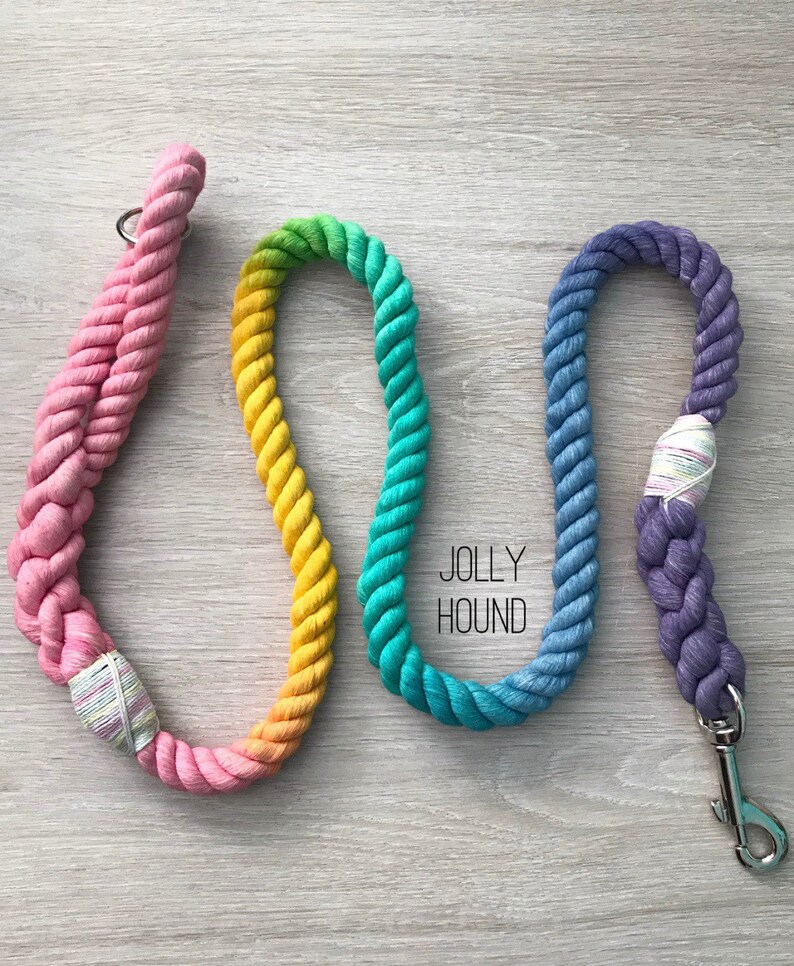 May include: Three colorful rope dog leashes with a rainbow ombre effect. The leashes are pink, yellow, green, and blue. The leashes have a metal clasp and are labeled "Jolly Hound".