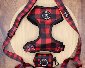 May include: A red and black buffalo plaid pet harness, matching leash, and waste bag dispenser. Each item features a circular black patch with the white text Jolly Hound and a paw print icon. The harness has black trim and plastic buckles.