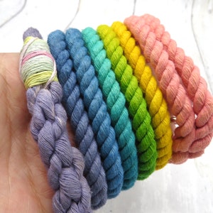 May include: A set of six colorful cotton rope bracelets in shades of purple, blue, teal, green, yellow, and pink.