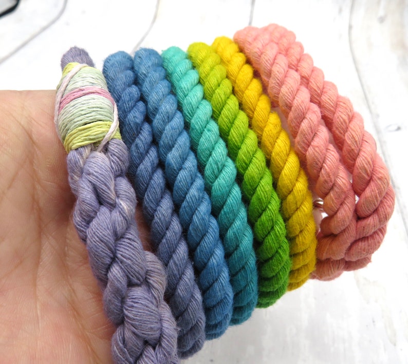 May include: A set of six colorful cotton rope bracelets in shades of purple, blue, teal, green, yellow, and pink.