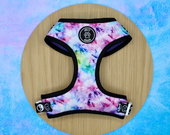 May include: A dog harness with a tie-dye pattern in shades of pink, blue, and green. The harness has black trim and adjustable straps. A circular patch with the text "JOLLY HOUND" and a paw print logo is centered on the harness.