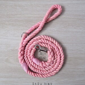 May include: A pink cotton rope dog leash with a silver clip and a tag that says "Jolly Hound". The leash is coiled up on a wooden surface and the text "BABY PINK" is printed below the leash.