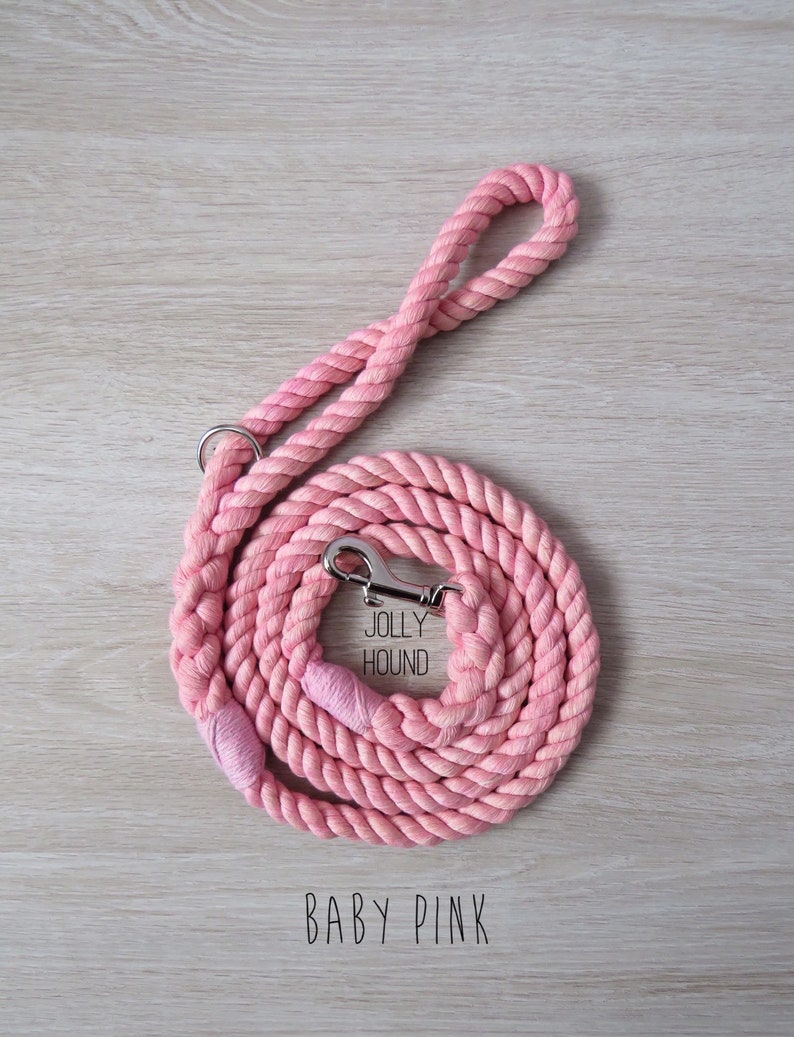 May include: A pink cotton rope dog leash with a silver clip and a tag that says "Jolly Hound". The leash is coiled up on a wooden surface and the text "BABY PINK" is printed below the leash.