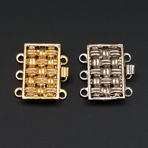 Puede incluir: Dos cierres metálicos para la elaboración de joyas. Uno es dorado y el otro plateado. Ambos tienen un diseño tejido y cuatro lazos.