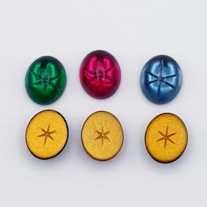 May include: Six oval-shaped cabochons with a star design. Three are green, red, and blue glass. Three are gold with a wood-like texture.