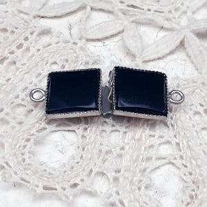 Op de afbeelding: Een zwarte vierkante sluiting met zilveren rand, perfect om een ​​toets van elegantie toe te voegen aan kettingen of armbanden.