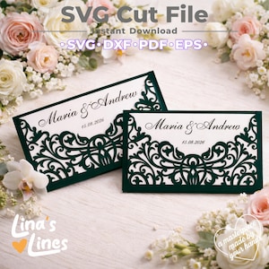 Peut inclure: Deux cartons de table de mariage découpés au laser vert foncé avec les noms "Maria & Andrew" et la date "15.08.2026" en écriture élégante. Les cartes présentent des motifs floraux complexes et sont posées sur un fond de fleurs blanches.