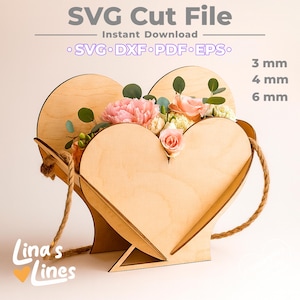 May include: A heart-shaped wooden flower box with a rope handle, filled with pink and peach flowers and greenery. The text "SVG Cut File" and "Instant Download" are at the top. The file formats are listed below. The thickness options are 3 mm, 4 mm, and 6 mm.