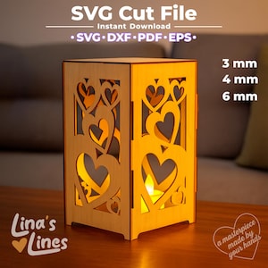 May include: A wooden lantern with heart-shaped cutouts, illuminated from within. The lantern is made of light-colored wood and features the text "SVG Cut File" and "Instant Download". The design includes the text "Lina's Lines" and "a masterpiece made by your hands".