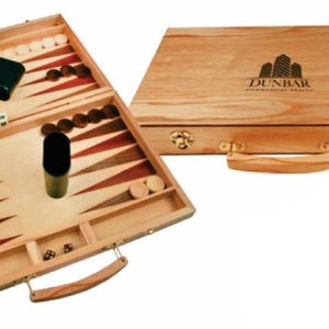 May include: A wooden backgammon set, open and closed. The open set displays a playing surface with red and brown triangles, white and brown game pieces, dice, and a dice cup. The closed set has a handle and the text "DUNBAR PROFESSIONAL REALTY".