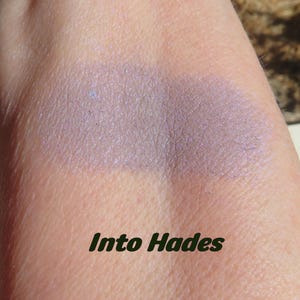 May include: A close-up of a light purple eyeshadow swatch on skin. The eyeshadow has a shimmery finish. The text "Into Hades" is written below the swatch.