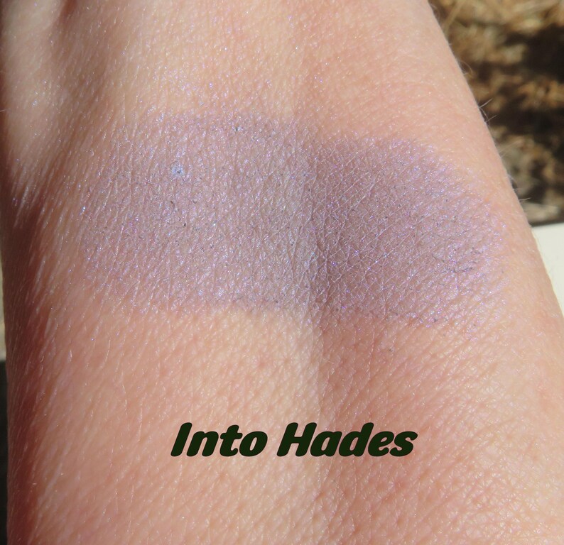 May include: A close-up of a light purple eyeshadow swatch on skin. The eyeshadow has a shimmery finish. The text "Into Hades" is written below the swatch.