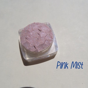 Puede incluir: Un pequeño recipiente transparente lleno de un polvo rosa claro brillante. La etiqueta dice "Pink Mist".