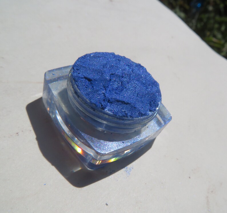 May include: A small, clear container filled with a bright blue glitter eyeshadow. The container is made of plastic and has a clear lid.