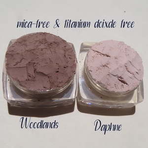Peut inclure: Deux petits contenants de poudre de maquillage min&eacute;rale en vrac. Le contenant de gauche est &eacute;tiquet&eacute; "Woodlands" et contient une poudre brune. Le contenant de droite est &eacute;tiquet&eacute; "Daphne" et contient une poudre rose clair. Le texte "mica-free & titanium dioxide free" est imprim&eacute; au-dessus des contenants.