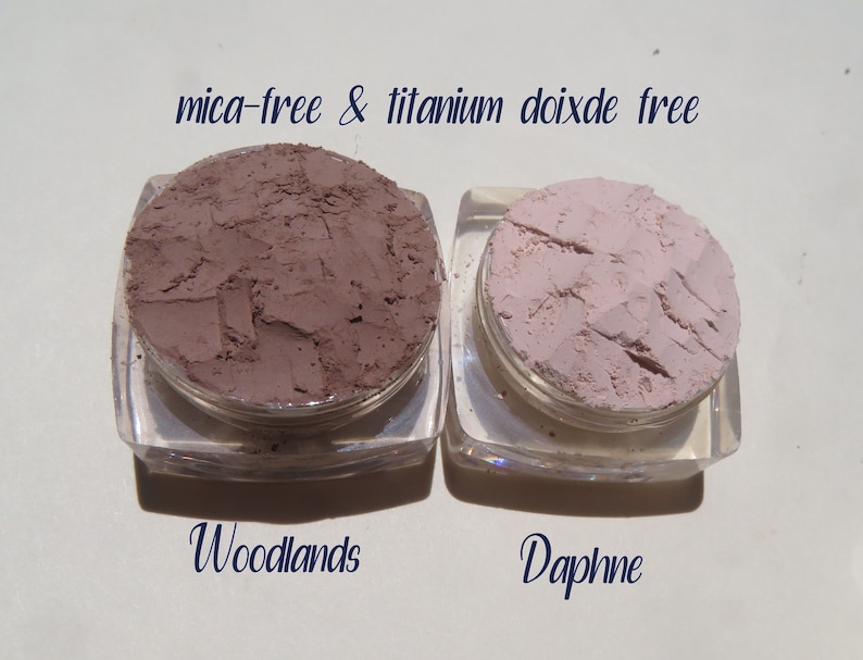 Peut inclure: Deux petits contenants de poudre de maquillage min&eacute;rale en vrac. Le contenant de gauche est &eacute;tiquet&eacute; "Woodlands" et contient une poudre brune. Le contenant de droite est &eacute;tiquet&eacute; "Daphne" et contient une poudre rose clair. Le texte "mica-free & titanium dioxide free" est imprim&eacute; au-dessus des contenants.
