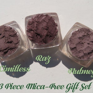 May include: Three square clear jars containing dark purple powder, labeled Limitless, Raz, and Nutmeg. The text 3 Piece Mica-Free Gift Set is printed below the jars. Each jar holds a textured, matte-finish cosmetic powder in a deep plum shade.