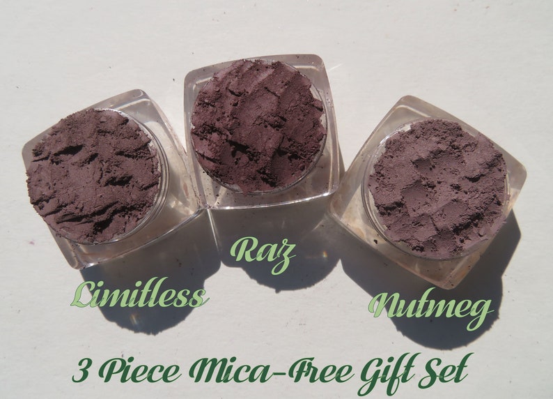 May include: Three square clear jars containing dark purple powder, labeled Limitless, Raz, and Nutmeg. The text 3 Piece Mica-Free Gift Set is printed below the jars. Each jar holds a textured, matte-finish cosmetic powder in a deep plum shade.